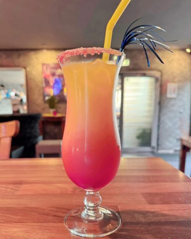 Lecker Cocktail Cocktail in einem hohen Glas mit orange-rotem Farbverlauf und einem bunten Strohhalm.